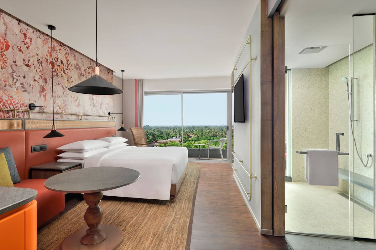 Une chambre d’hôtel moderne dotée d’un grand lit, d’un coin salon avec une table, d’un balcon avec vue et d’un espace douche.