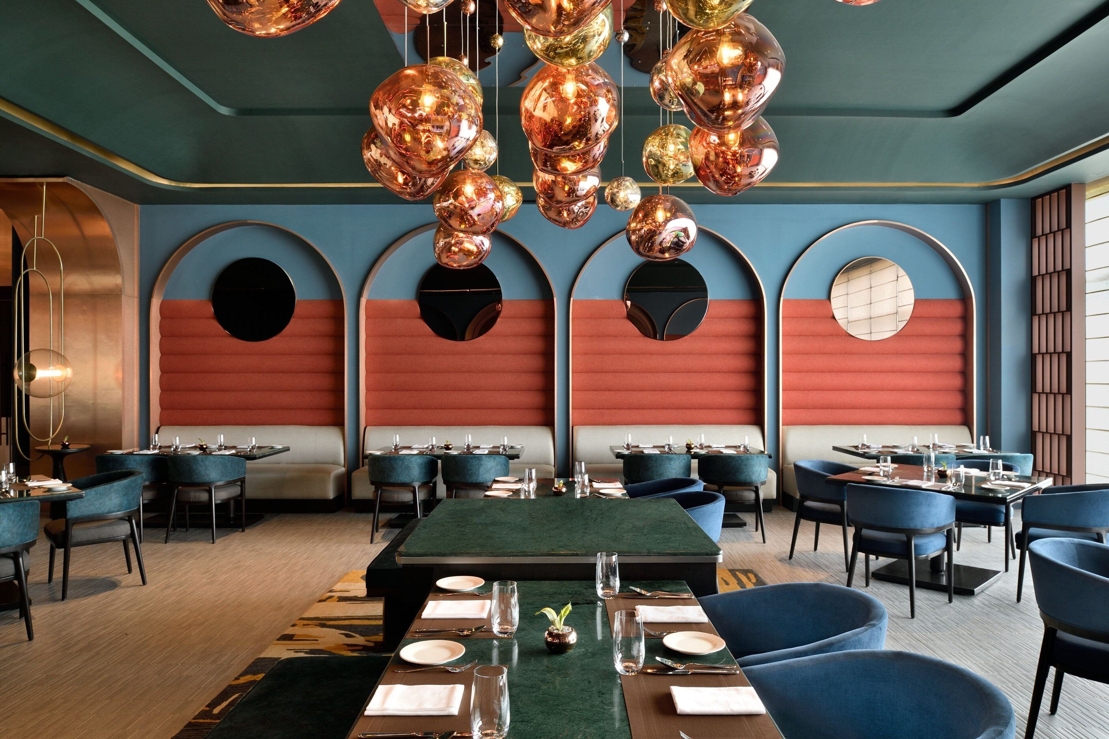 Een restaurant met ronde tafels, blauwe stoelen en een groen tapijt.