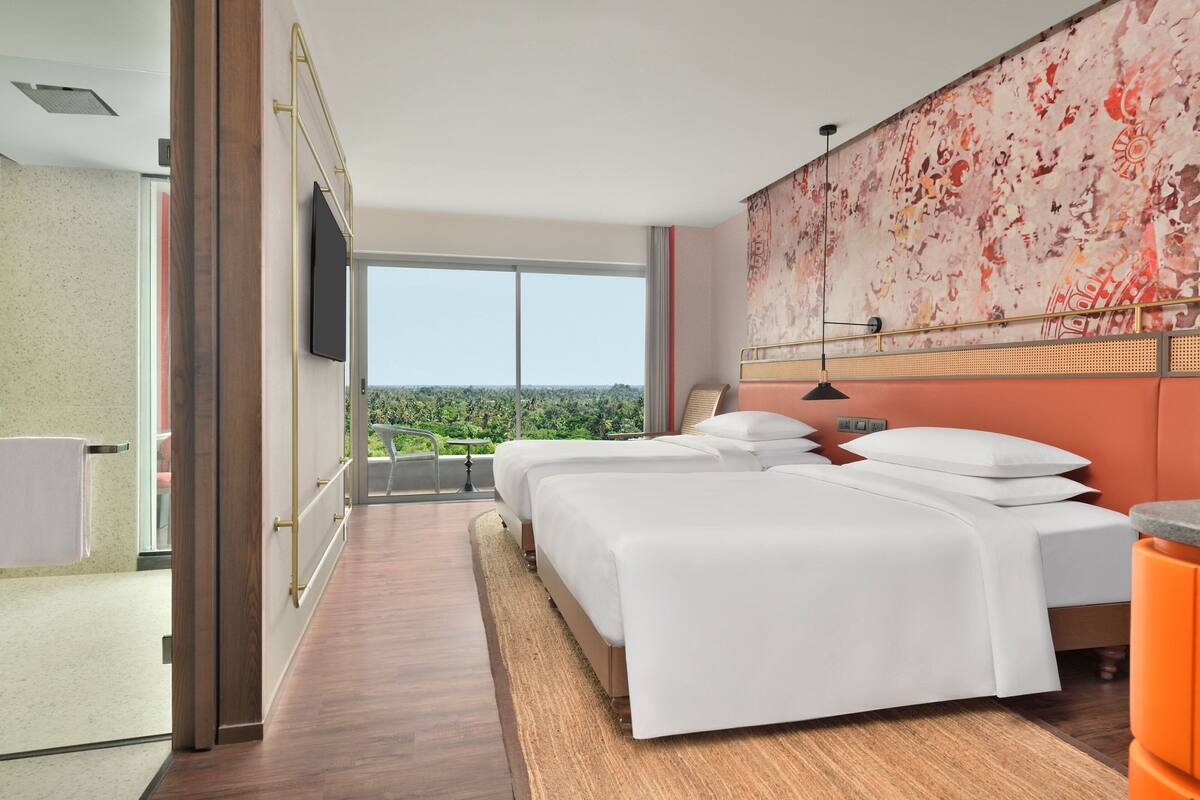 Une chambre d’hôtel avec deux lits, une grande fenêtre donnant sur la ville, et un design moderne avec un plancher en bois et un mur décoratif.