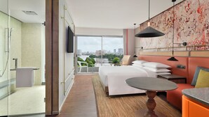 Een moderne hotelkamer met een groot bed, een kleine tafel, een bank, een televisie en een balkon met uitzicht over de stad.