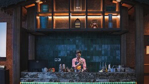 Een bar met een bartender, houten kasten vol flessen en een verlichte toonbank.