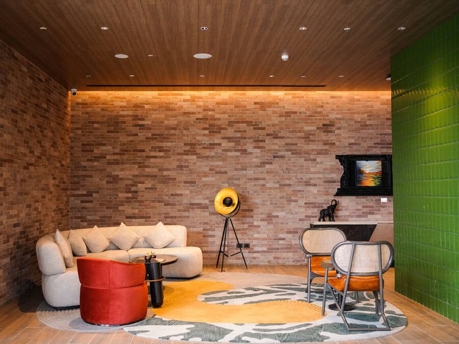 Una sala de estar moderna con pared de ladrillo, un sofá, un reposapiés rojo, una lámpara de pie y una pared verde de acento.