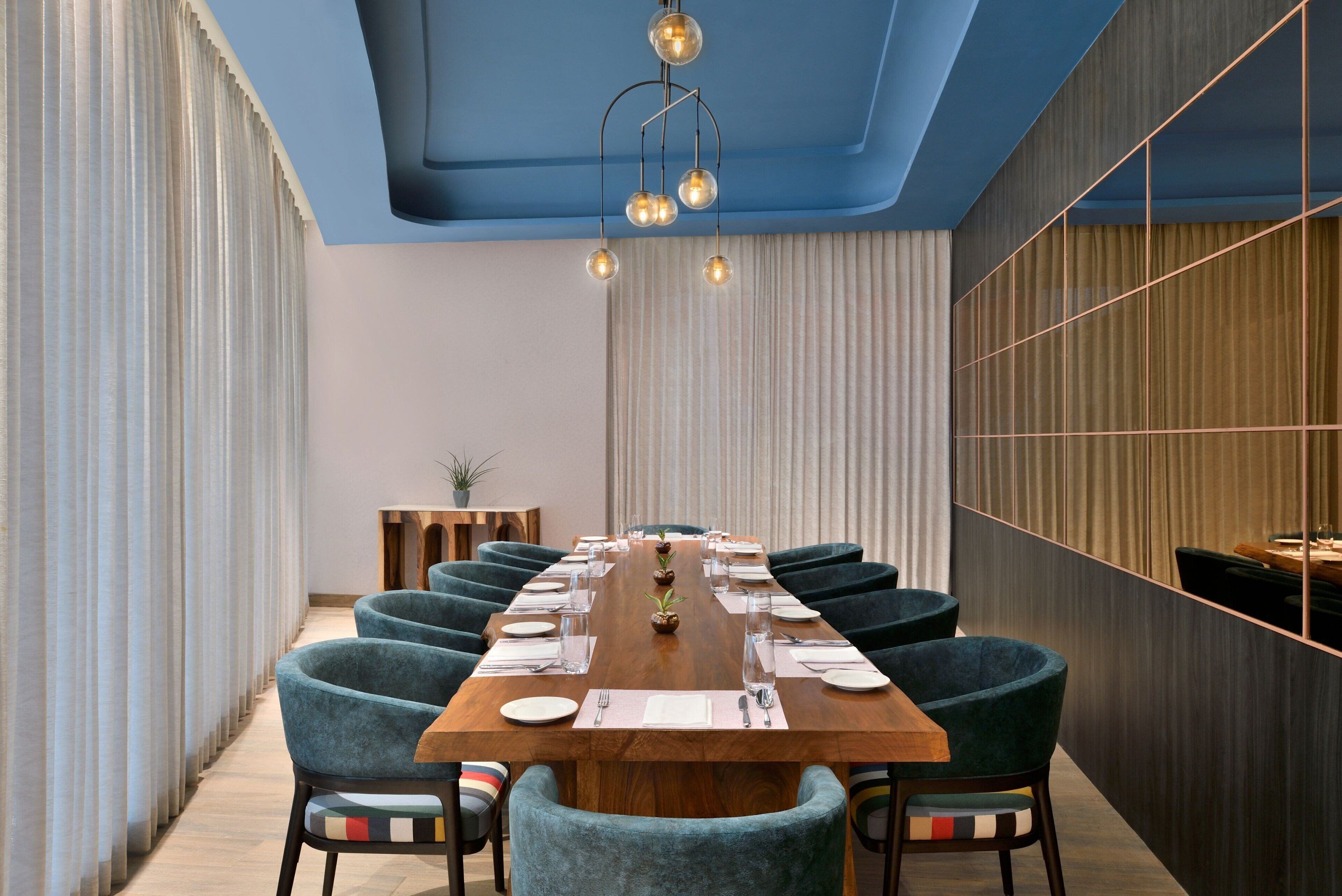 A conference room with a long wooden table, teal upholstered chairs, and a modern ceiling design.