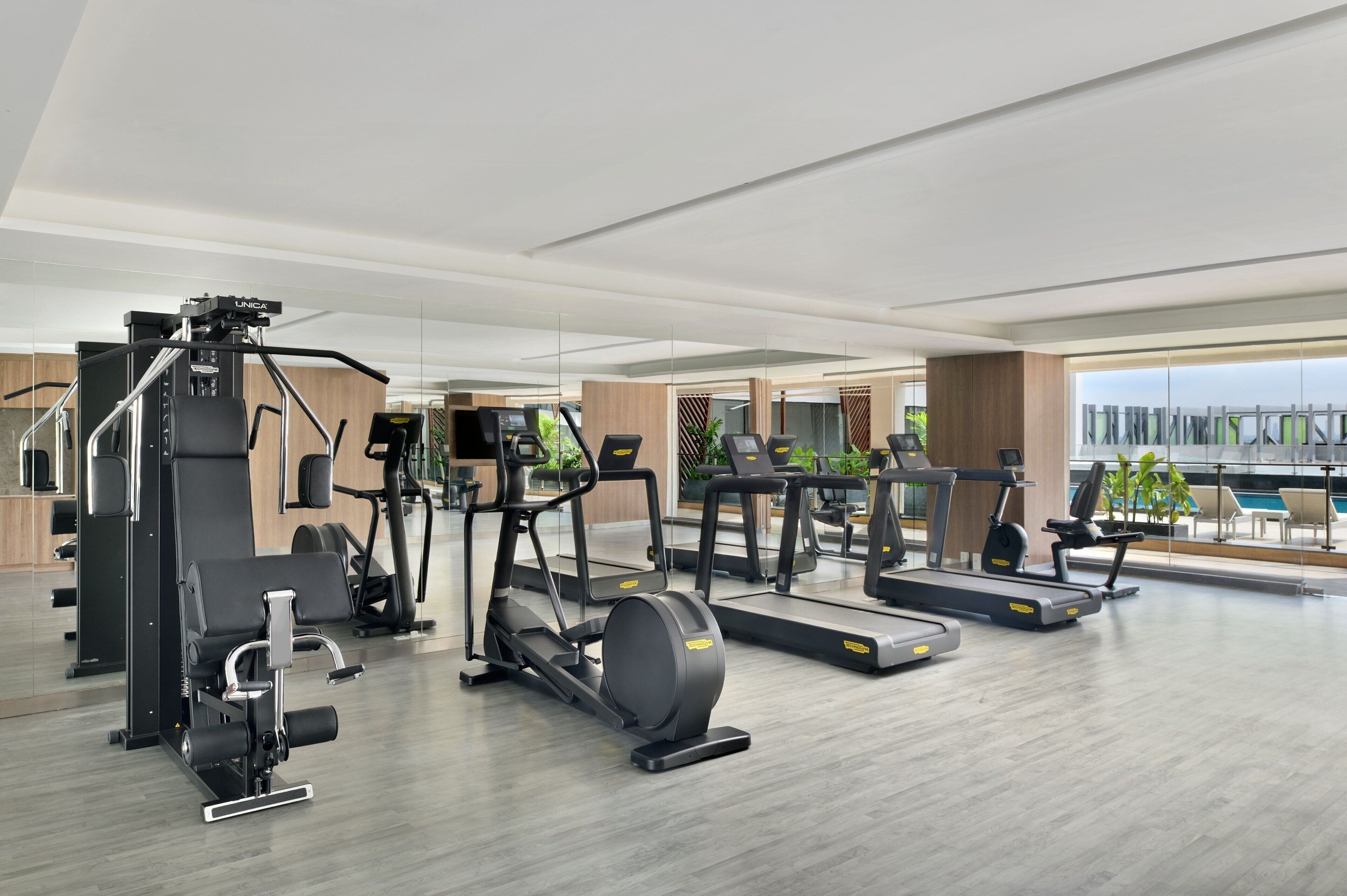 A modern gym with various exercise equipment, large windows, and a view of the outdoors.