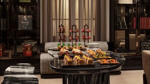 Un salón lujoso con una mesa de centro de mármol que presenta una variedad de postres y aperitivos, un sofá y una estantería con libros y objetos decorativos.