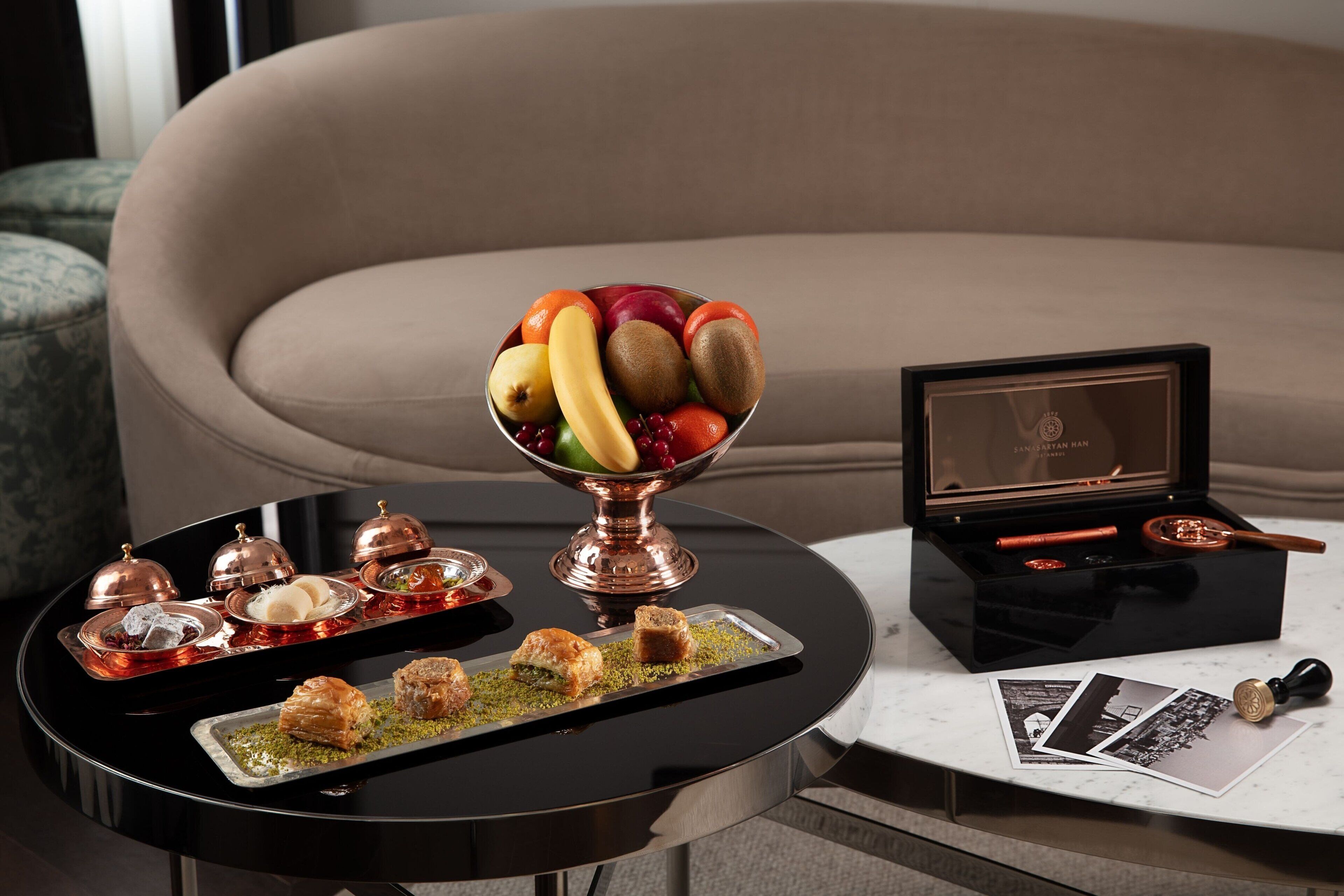 A dining table with a fruit bowl, dessert trays, and a black box with a framed photo and a pen.