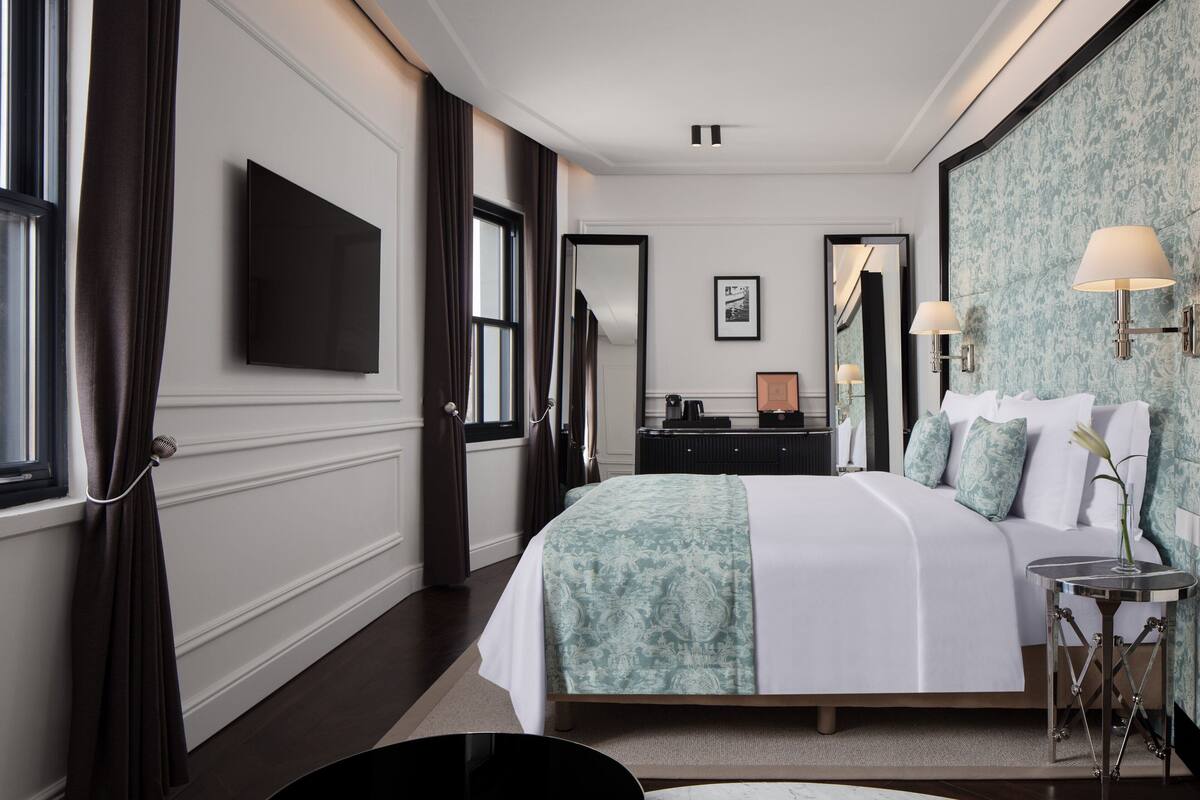 Una habitación de hotel con una cama grande, un televisor montado en la pared, un aparador y un espejo.