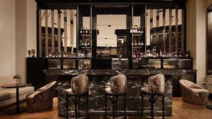 Zona de bar con encimera de mármol, taburetes y una variedad de botellas y vasos.