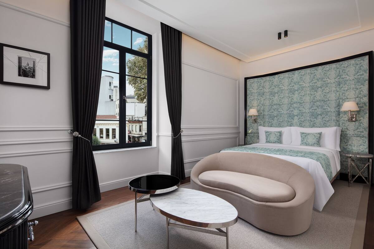 Una habitación de hotel moderna con una cama grande, un sofá curvo, una pequeña mesa redonda y vistas al exterior.