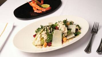 Un plato blanco con ensalada, un plato negro con camarones, y un tenedor sobre una mesa blanca.