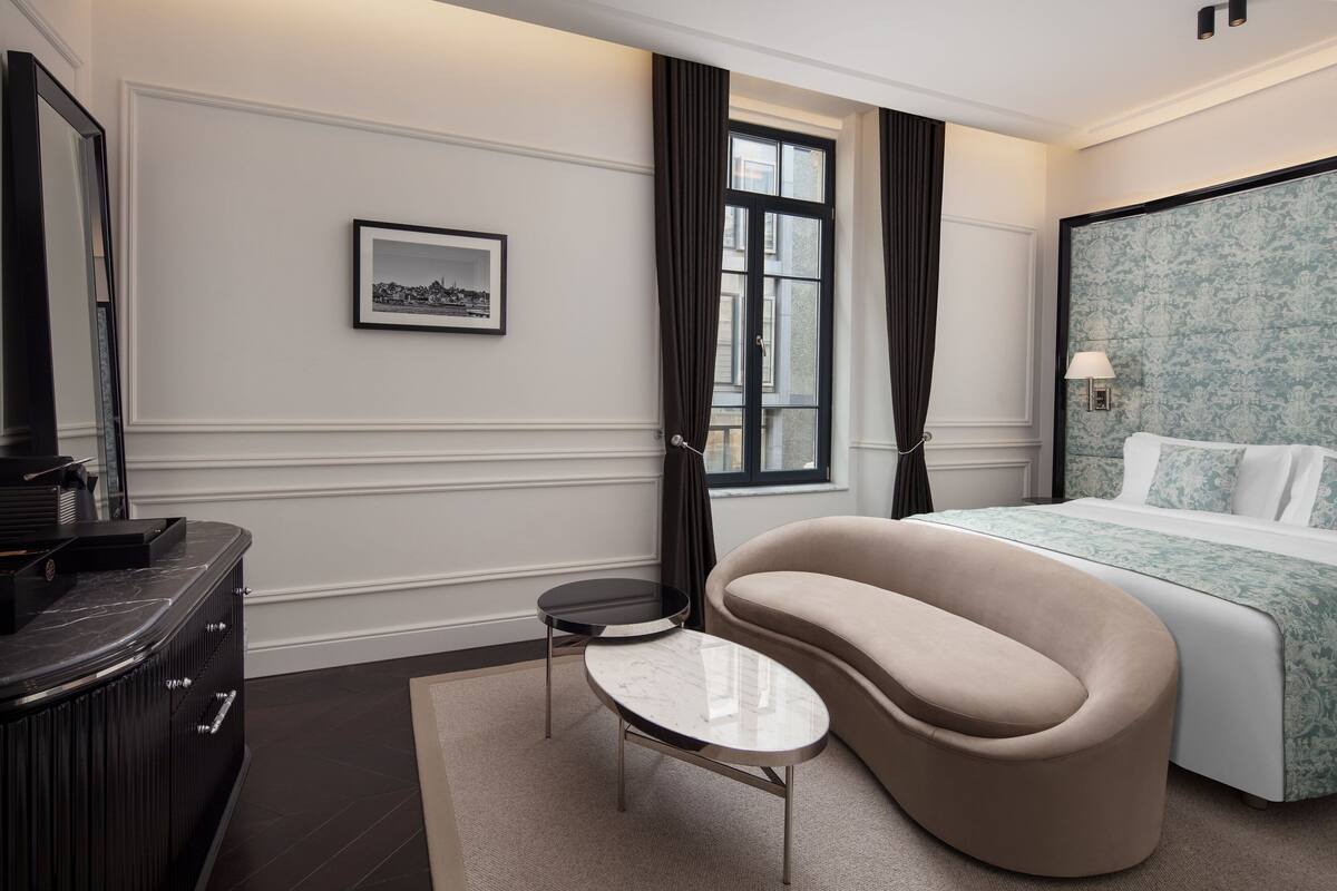 Habitación de hotel con cama, sofá, mesita, cómoda y un cuadro en la pared.