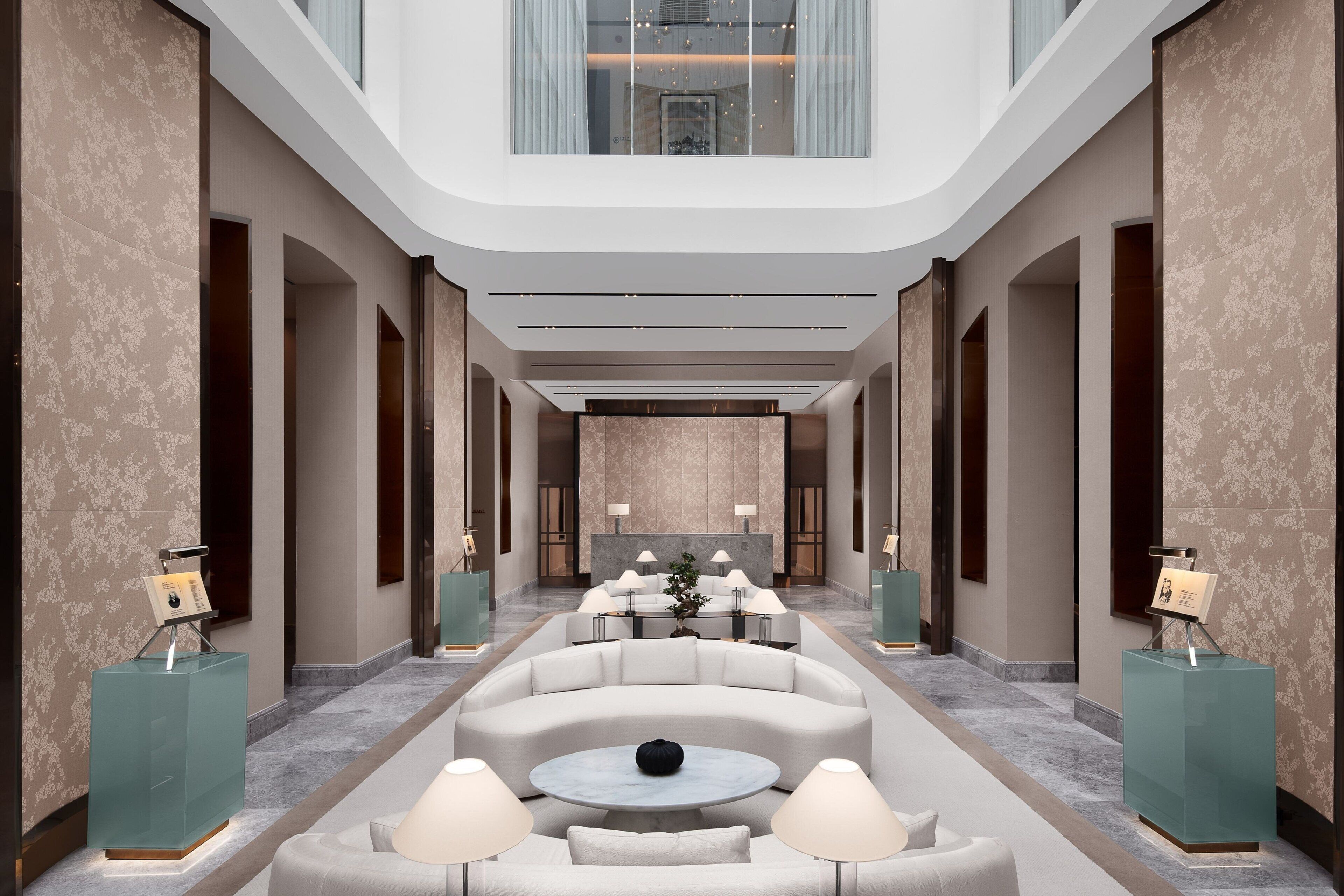 A modern hotel lobby with a central seating area, a reception desk, and a high ceiling with natural light.