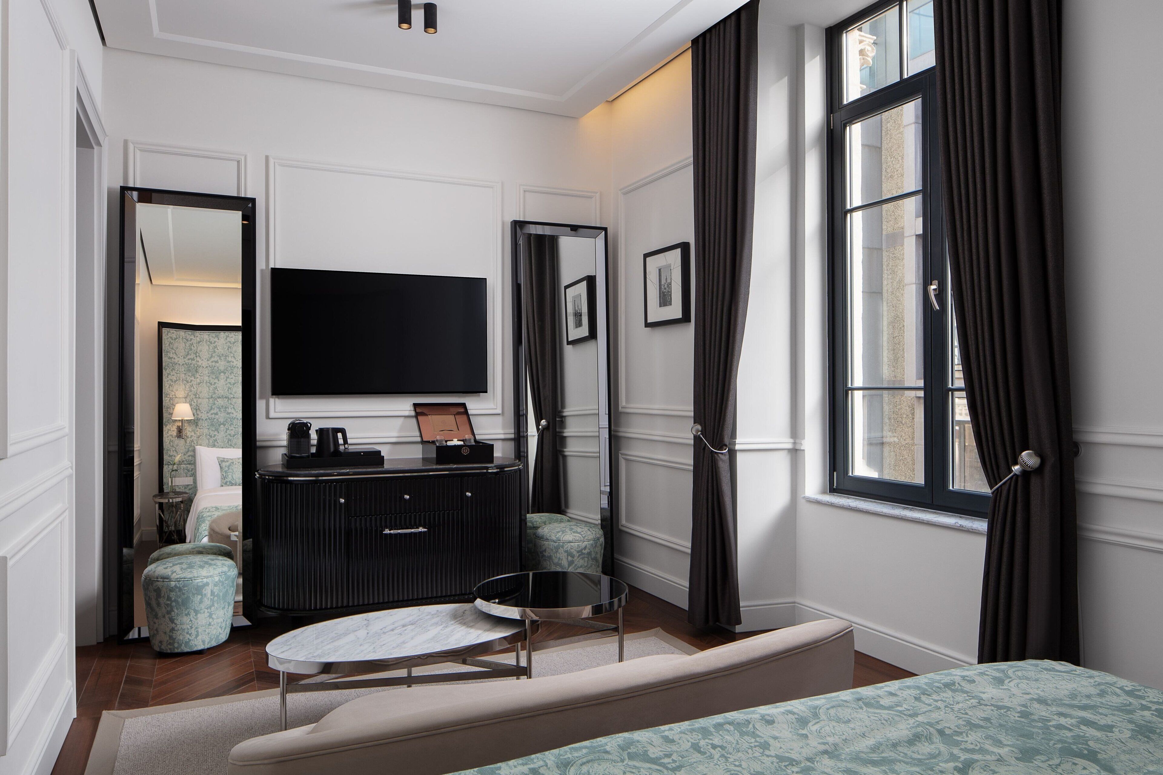 Un dormitorio moderno con una televisión de pantalla plana grande, un aparador negro, una mesa redonda y una cama con ropa de cama estampada.