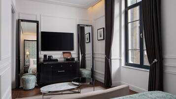 Un dormitorio moderno con una televisión de pantalla plana grande, un aparador negro, una mesa redonda y una cama con ropa de cama estampada.
