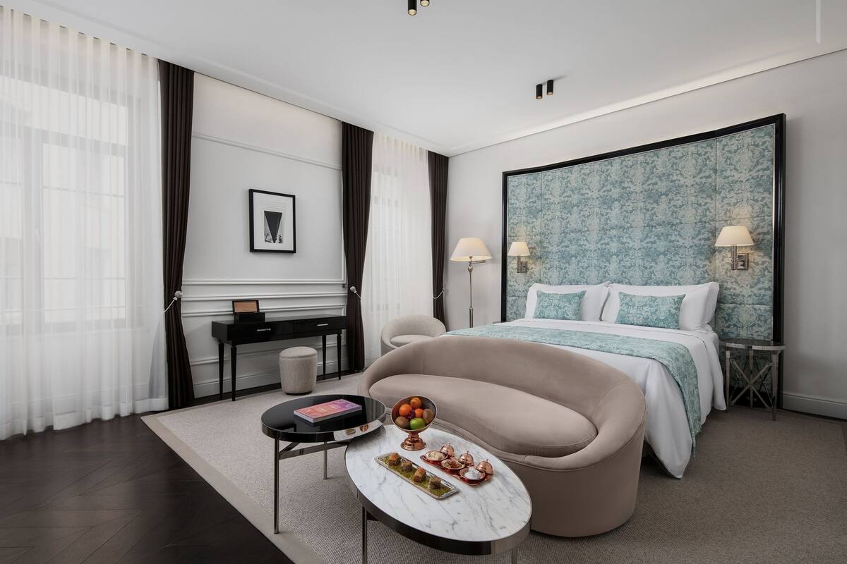 Una habitación de hotel moderna con una cama grande, un sofá, una mesita con un frutero y un escritorio con una lámpara.