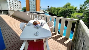 Un balcón con una mesa lista para comer, con vistas a una piscina y una vista de edificios y follaje.