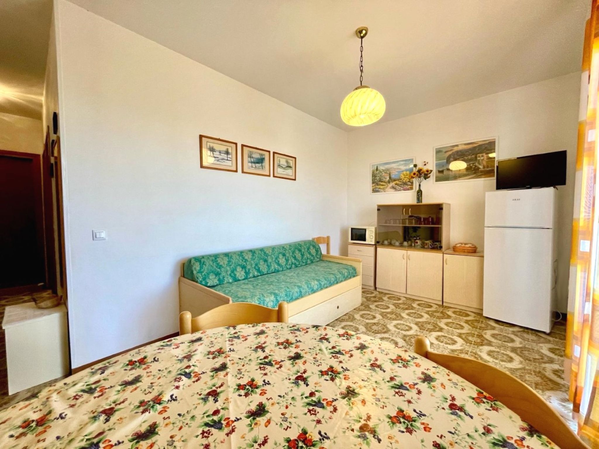 A bedroom with a bed, a sofa, a television, a refrigerator, and a small kitchen area.