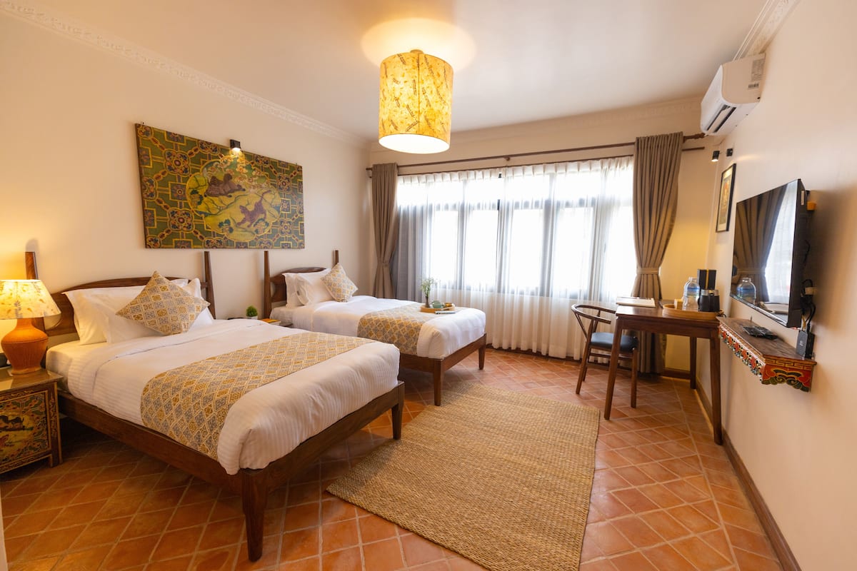 Una habitación de hotel con dos camas, un escritorio, un televisor y un ventanal con cortinas.