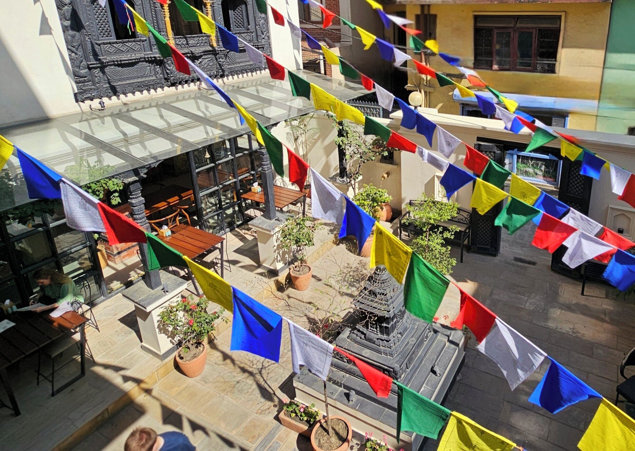 A courtyard with a traditional building, outdoor seating, and colorful flags.