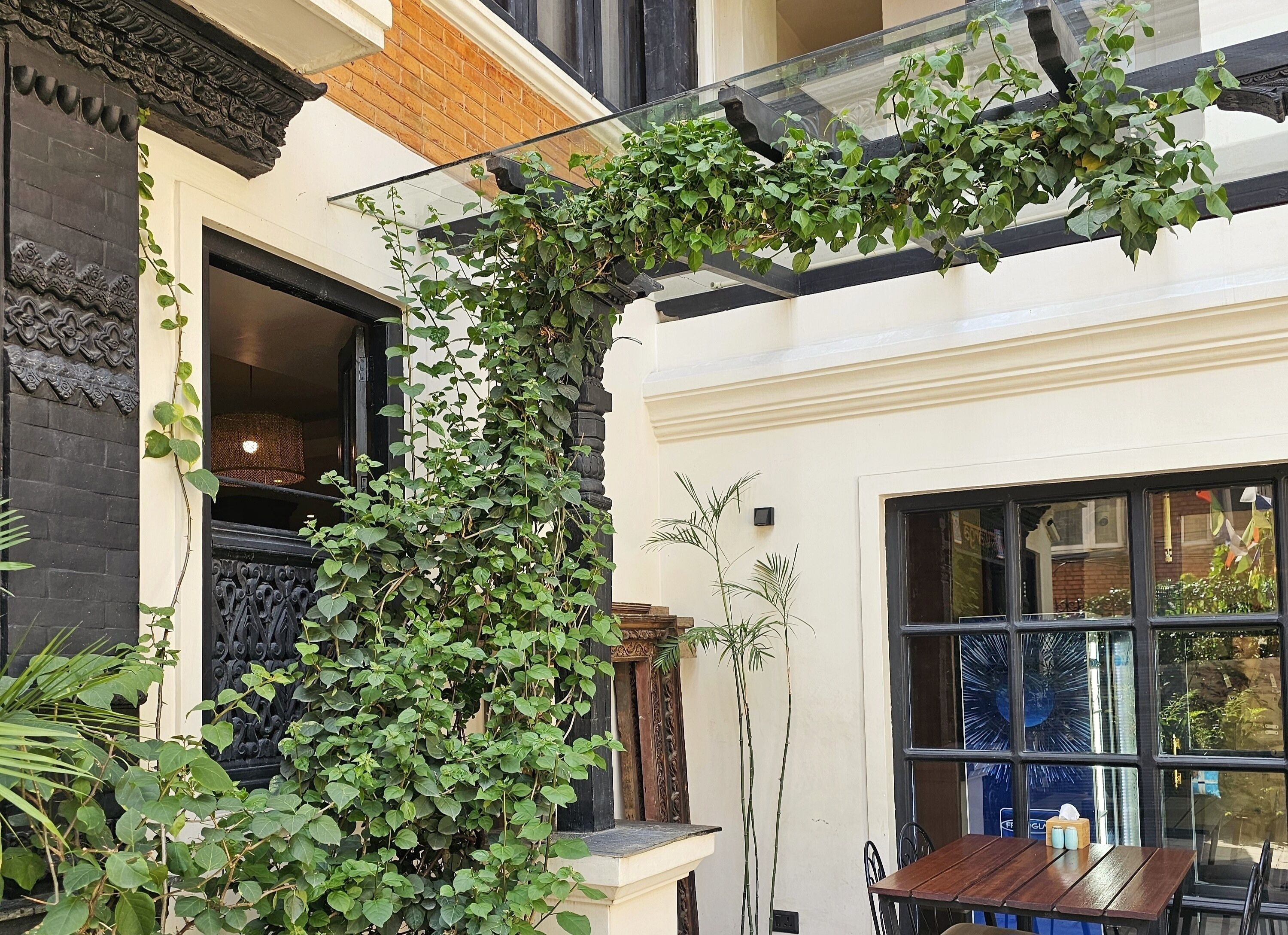 Une cour avec une table et des chaises en bois, une balustrade en verre et un portail en fer forgé noir.