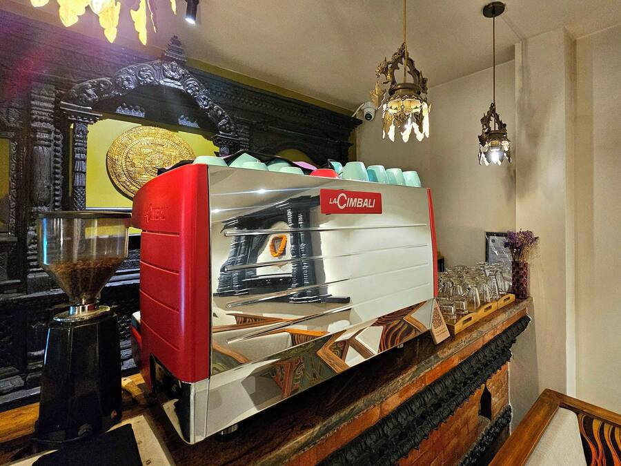 A coffee machine with a red and white design, a coffee grinder, and a decorative wall with an ornate arch and a chandelier.