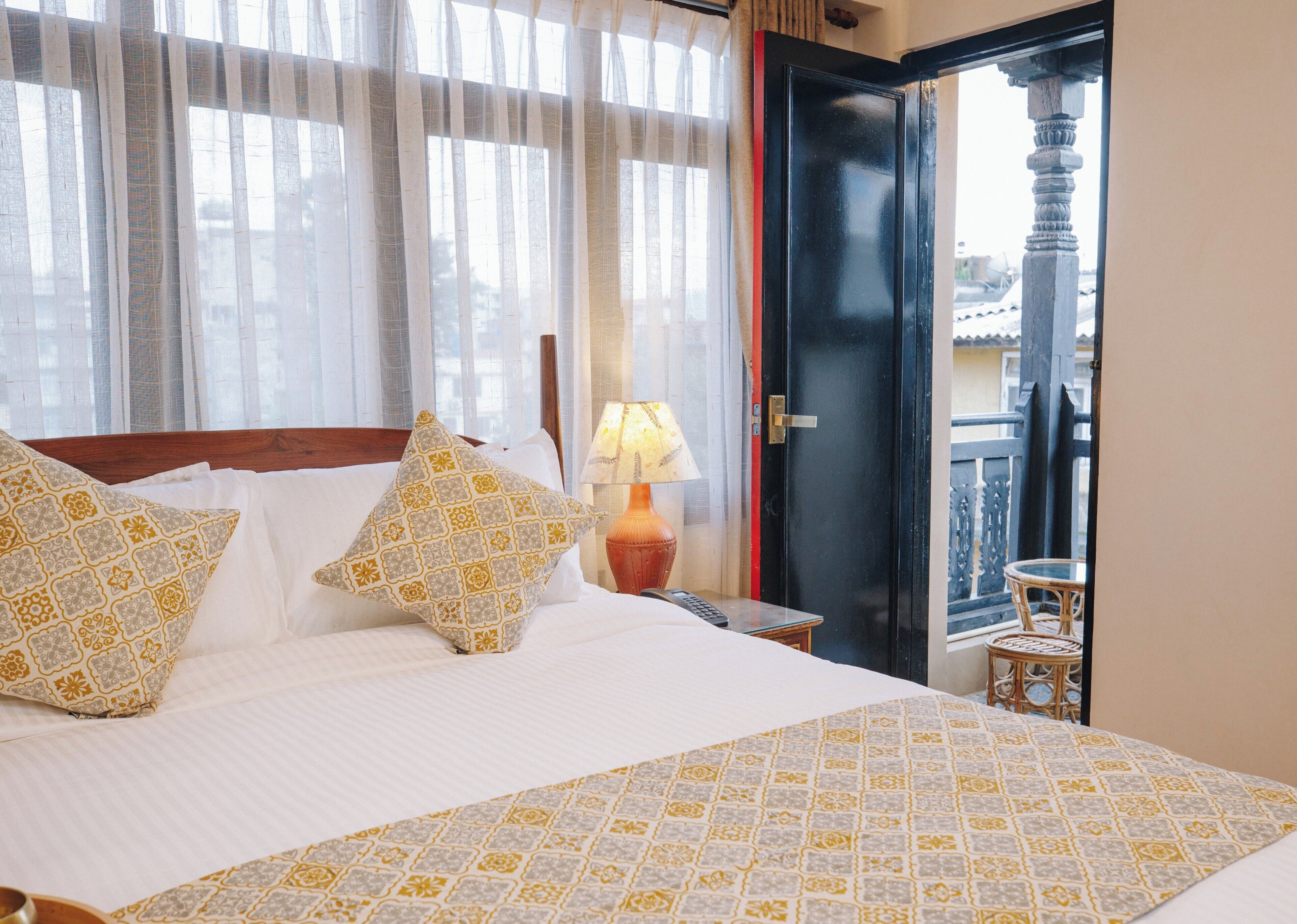 A hotel room with a bed, pillows, a nightstand, a lamp, and a view of the outside balcony.