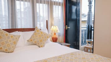 A hotel room with a bed, pillows, a nightstand, a lamp, and a view of the outside balcony.