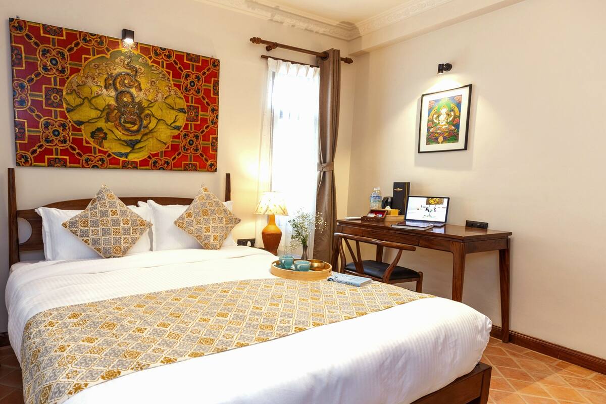 Habitación de hotel con una cama grande, un escritorio con una computadora portátil, un cuadro decorativo y una ventana con cortinas.