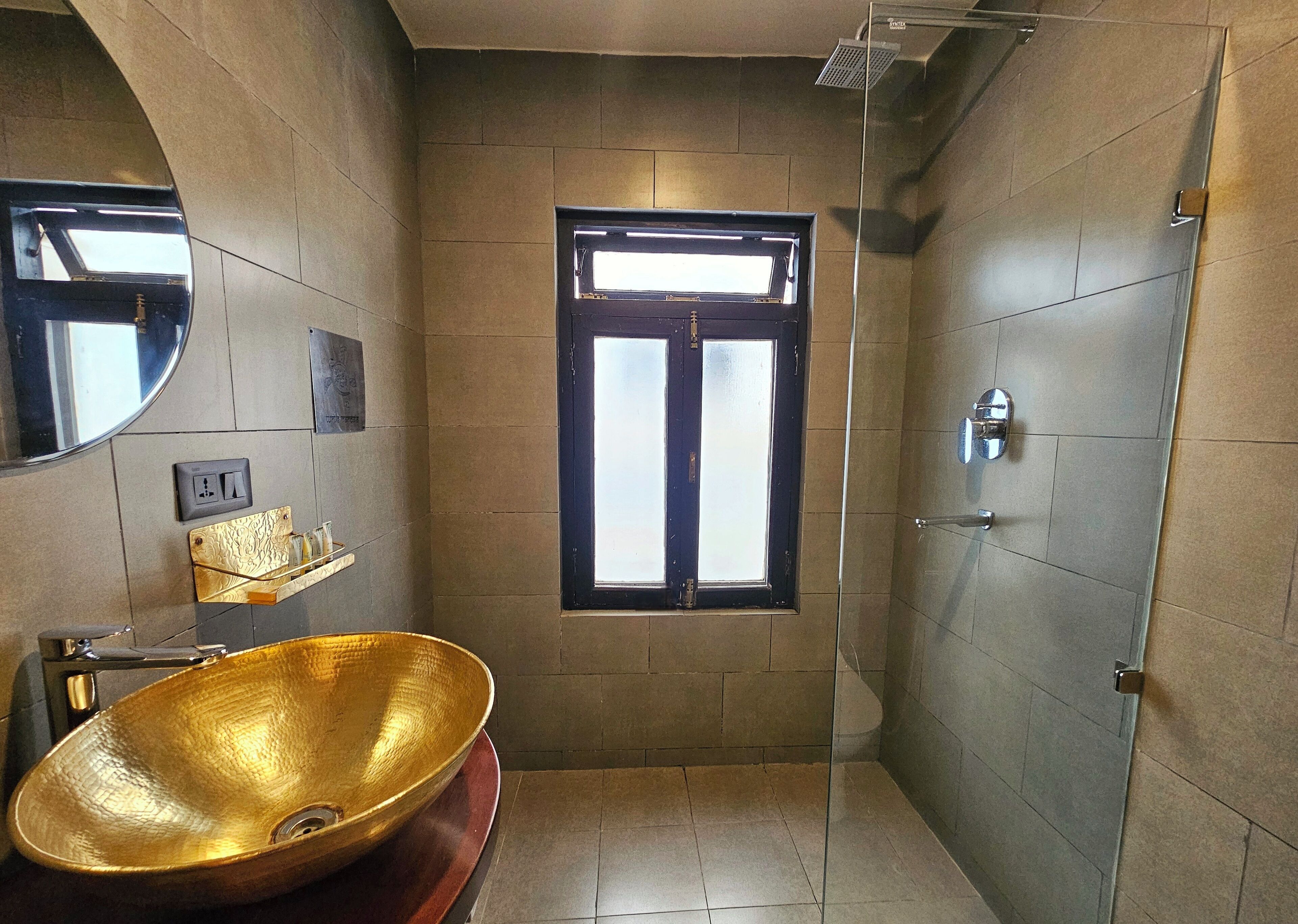 A bathroom with a large golden sink, a mirror, a window, and a shower area.