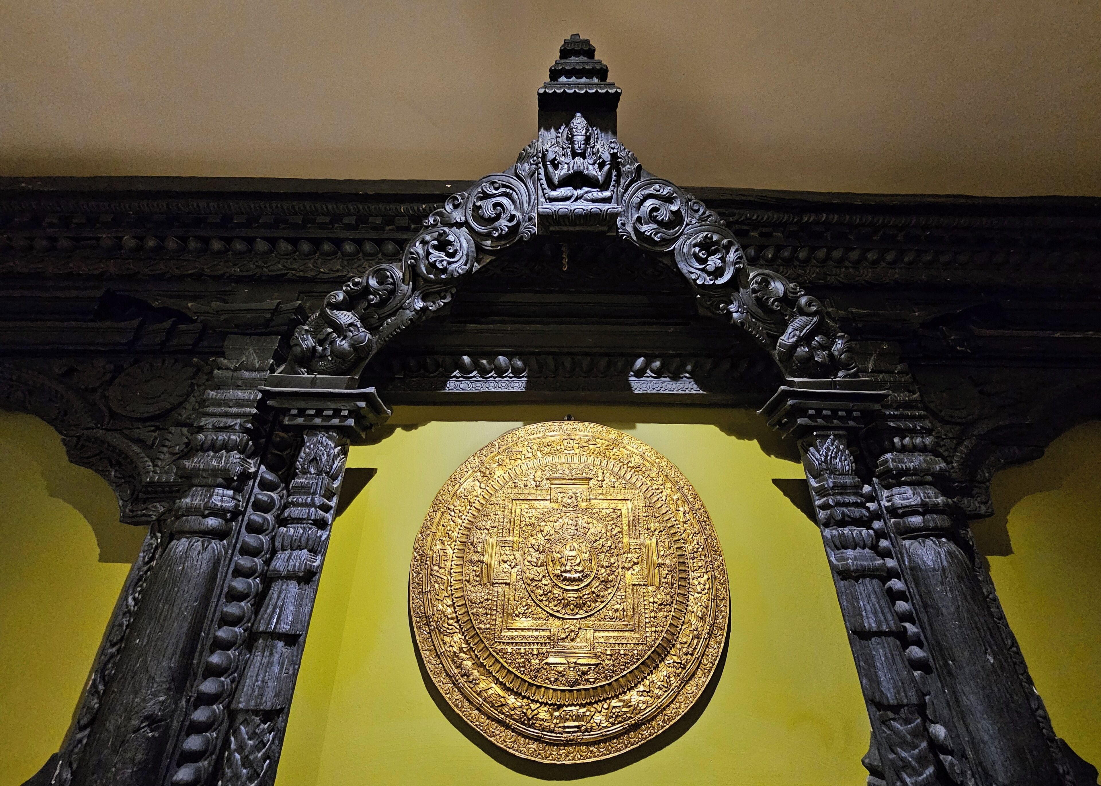 A detailed golden emblem set within an ornate black frame against a yellow wall.