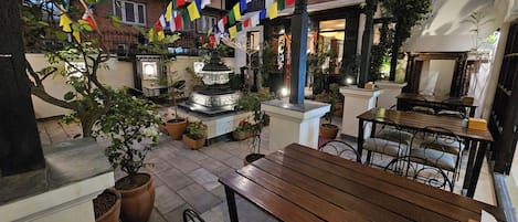 An outdoor patio area with a wooden bench, potted plants, and a fountain.
