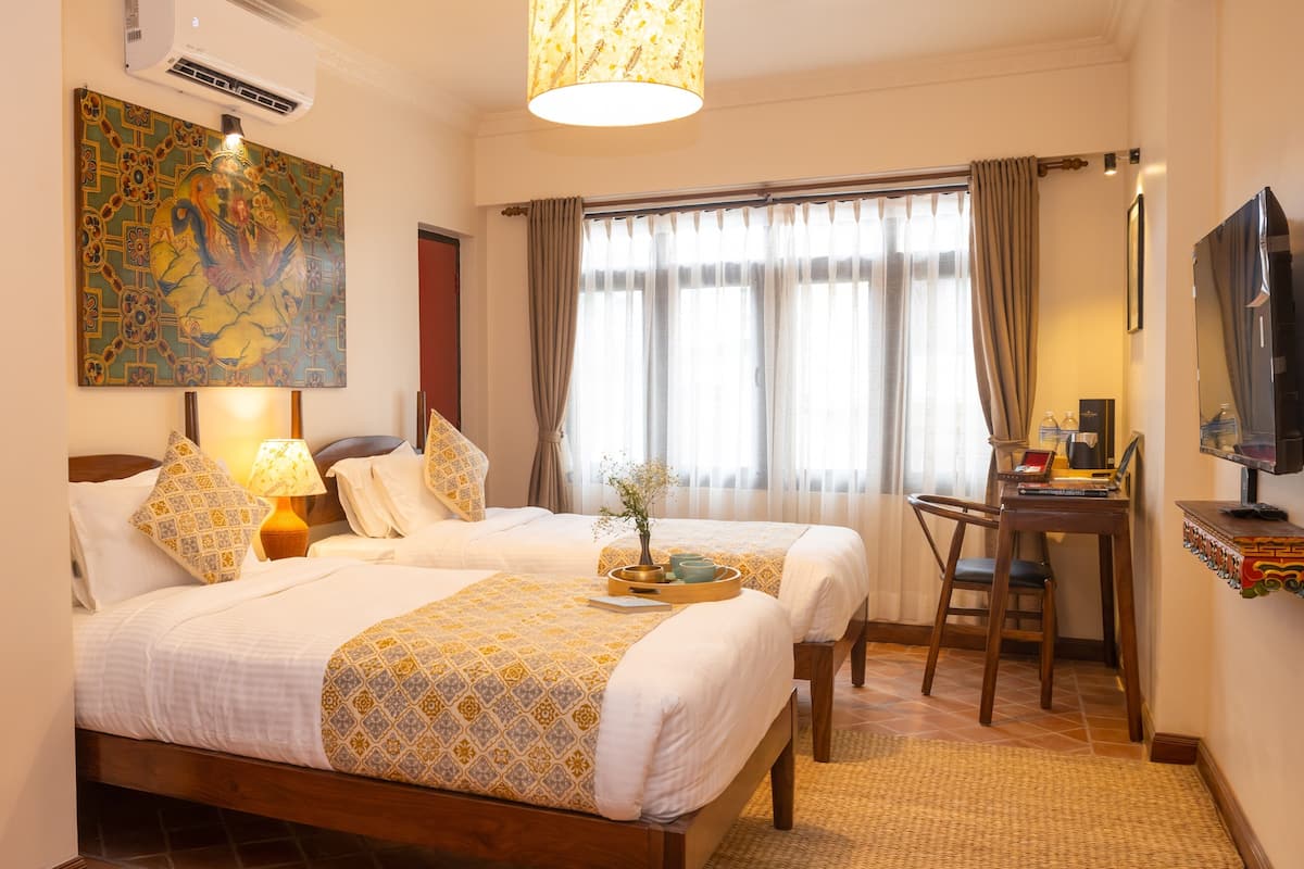 Habitación de hotel con dos camas, un escritorio, un televisor y un amplio ventanal con cortinas.