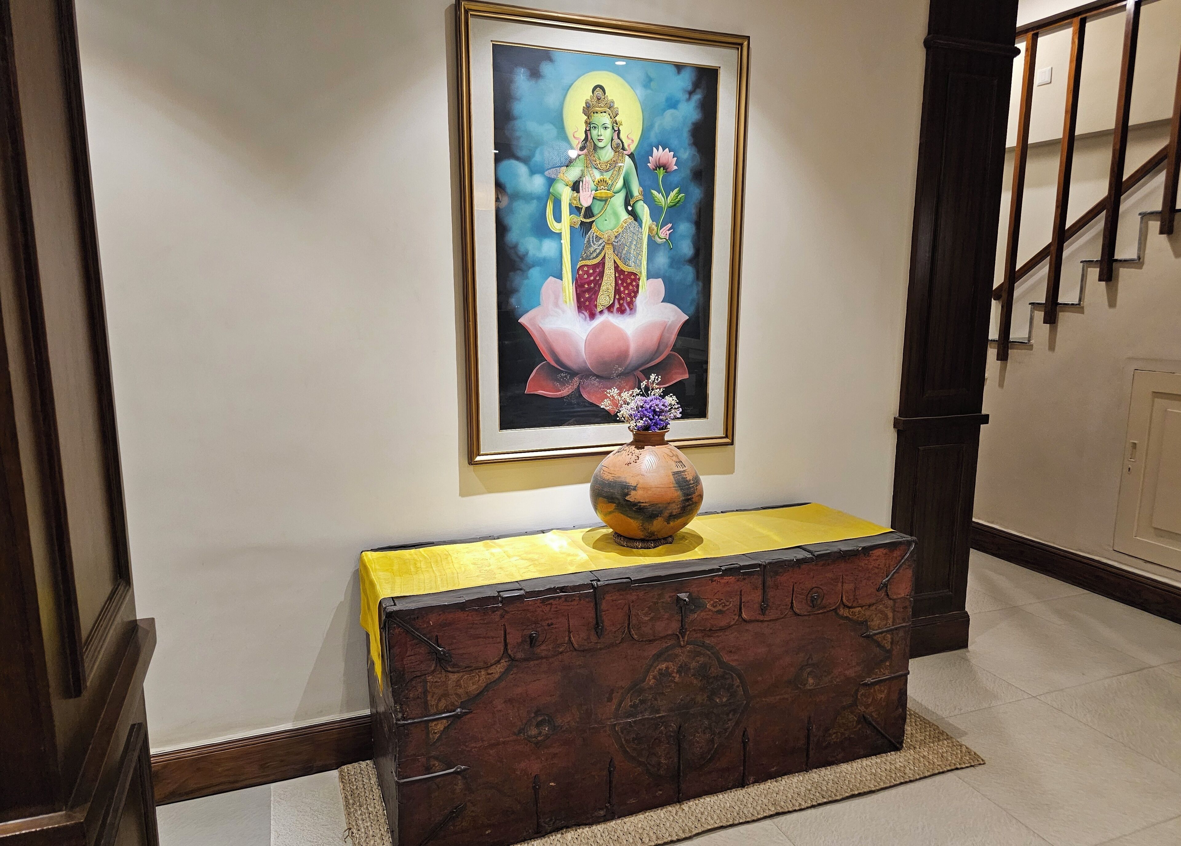 A staircase with a framed religious painting above a wooden chest with a vase of flowers.