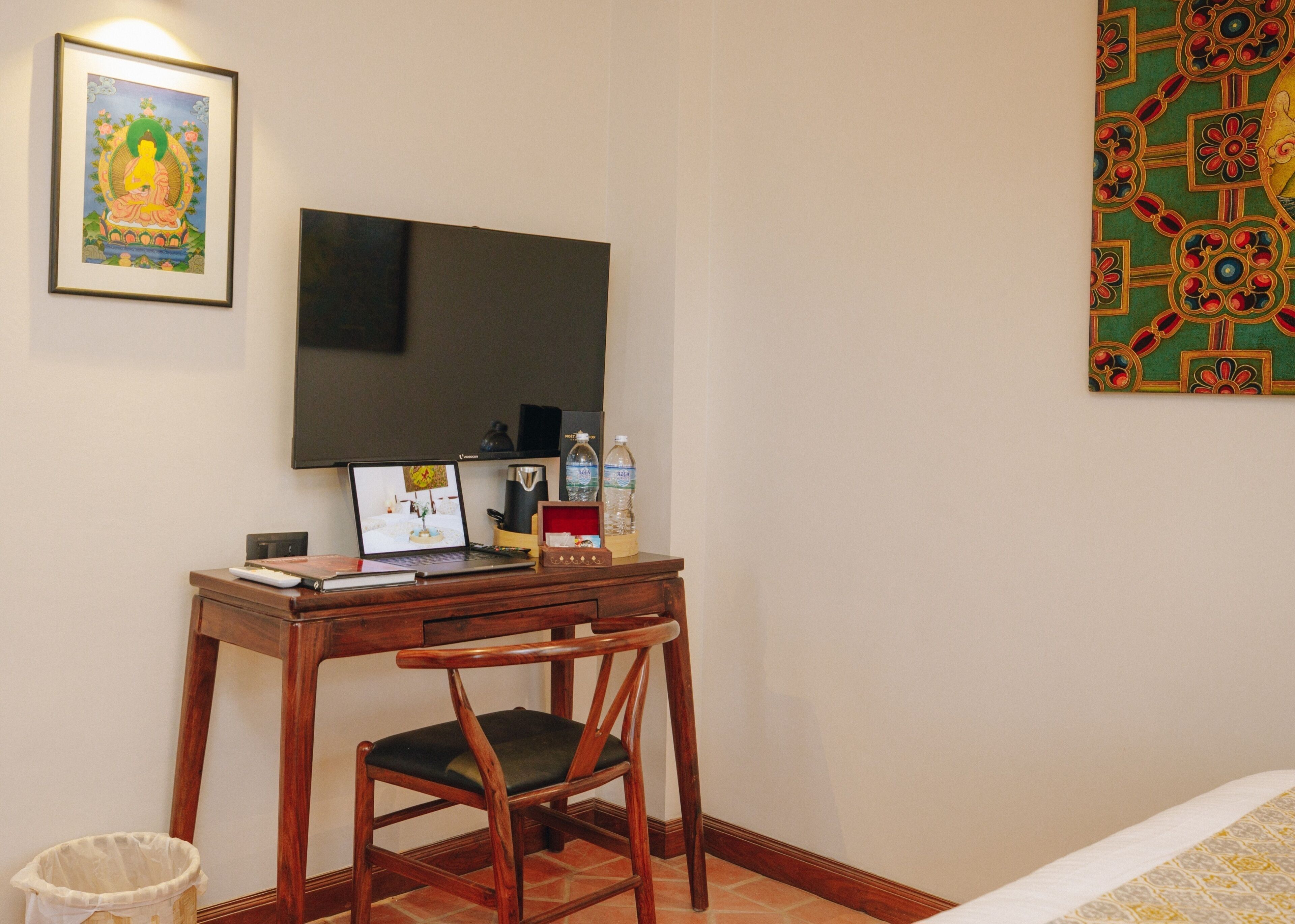 A room with a wooden desk, a chair, a television mounted on the wall, and a framed picture above the desk.