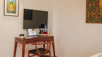 A room with a wooden desk, a chair, a television mounted on the wall, and a framed picture above the desk.
