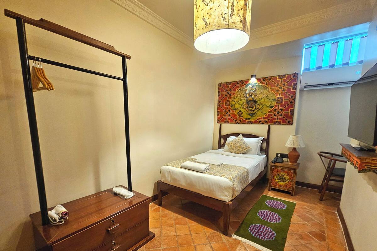 Un dormitorio con cama, una mesita de noche de madera, un escritorio con silla, una lámpara colgante y un aire acondicionado de pared.