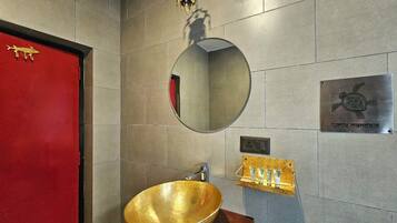 A bathroom with a round mirror, a gold bowl sink, a red door, and a plaque with a turtle design.
