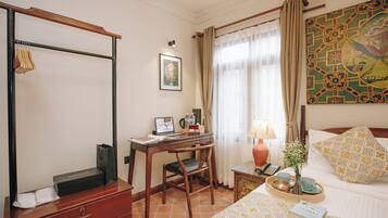Habitación de hotel con escritorio de madera, una laptop, una silla, una cama con almohadillas estampadas, una mesita de noche con lámpara y un cuadro en la pared.
