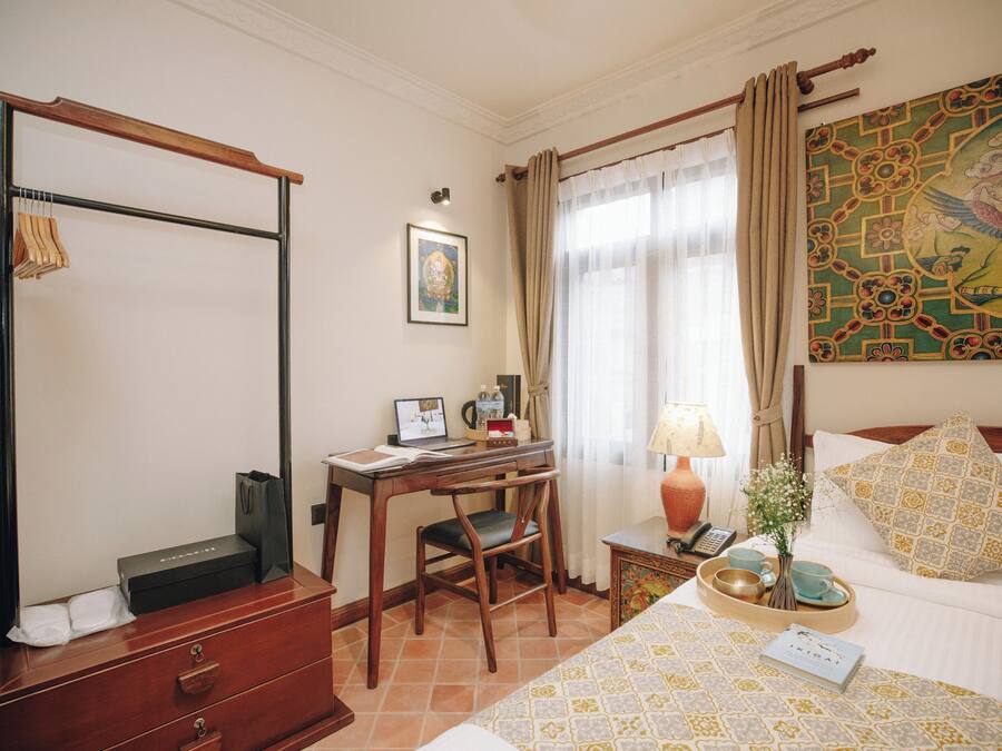 Habitación de hotel con escritorio de madera, una laptop, una silla, una cama con almohadillas estampadas, una mesita de noche con lámpara y un cuadro en la pared.