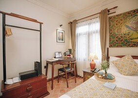 Habitación de hotel con escritorio de madera, una laptop, una silla, una cama con almohadillas estampadas, una mesita de noche con lámpara y un cuadro en la pared.