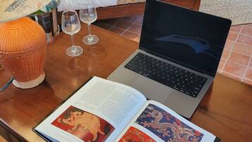 A laptop on a wooden table with two open books, a lamp, and three wine glasses.