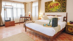 Una habitación de hotel con cama, escritorio, silla, lámpara y obras de arte.