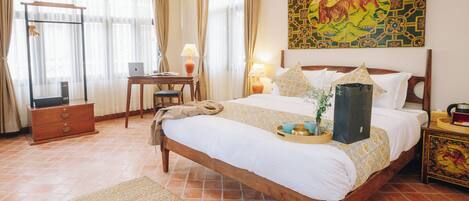 A hotel room with a bed, desk, chair, lamp, and artwork.