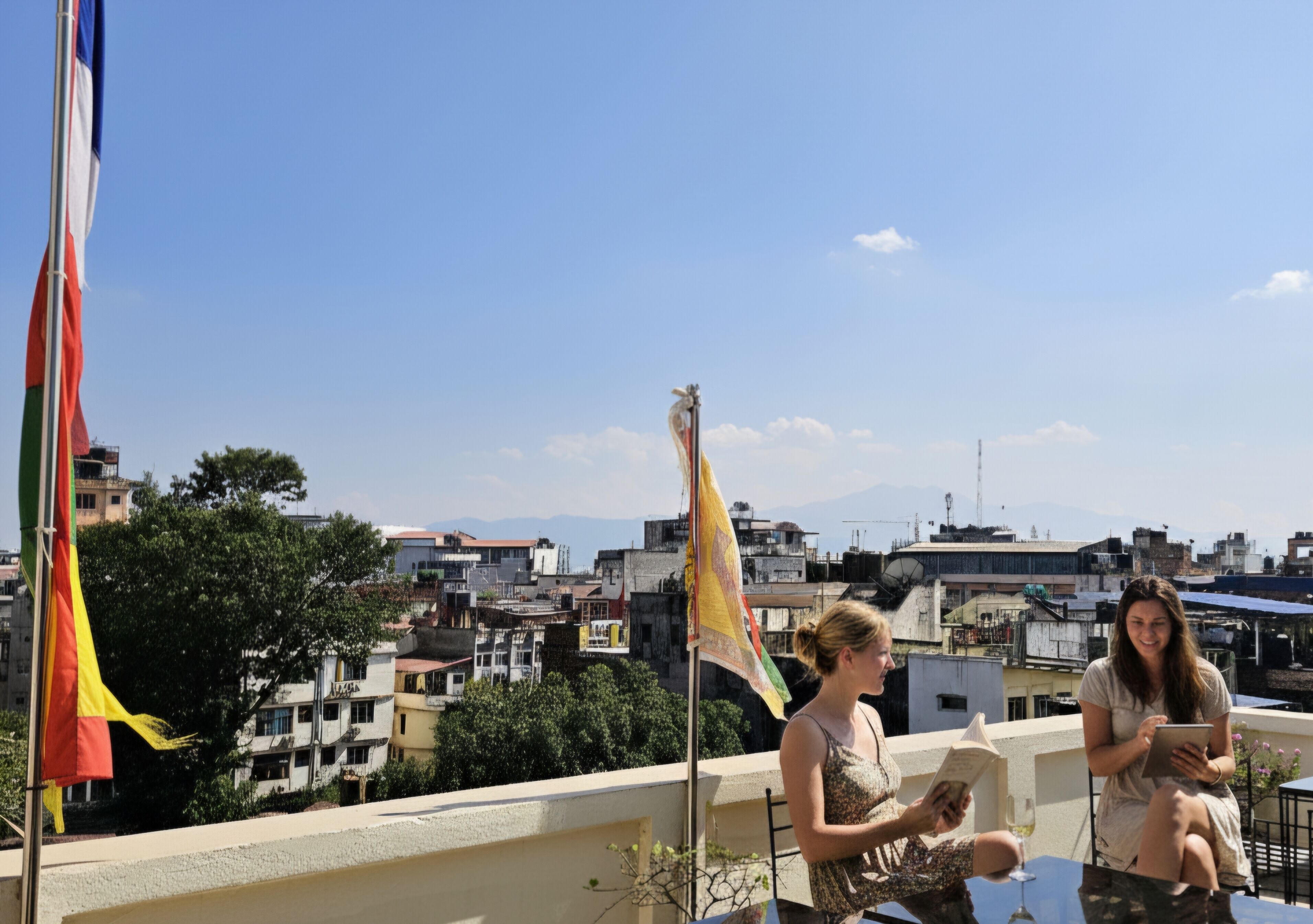 Terraza en la azotea con vistas a la ciudad, banderas y dos personas leyendo.