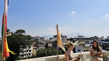 Terraza en la azotea con vistas a la ciudad, banderas y dos personas leyendo.