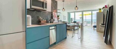 Una cocina moderna con microondas integrado, lavavajillas y una isla grande. Hay una zona de comedor con mesa y sillas, y vistas al océano a través de amplios ventanales.
