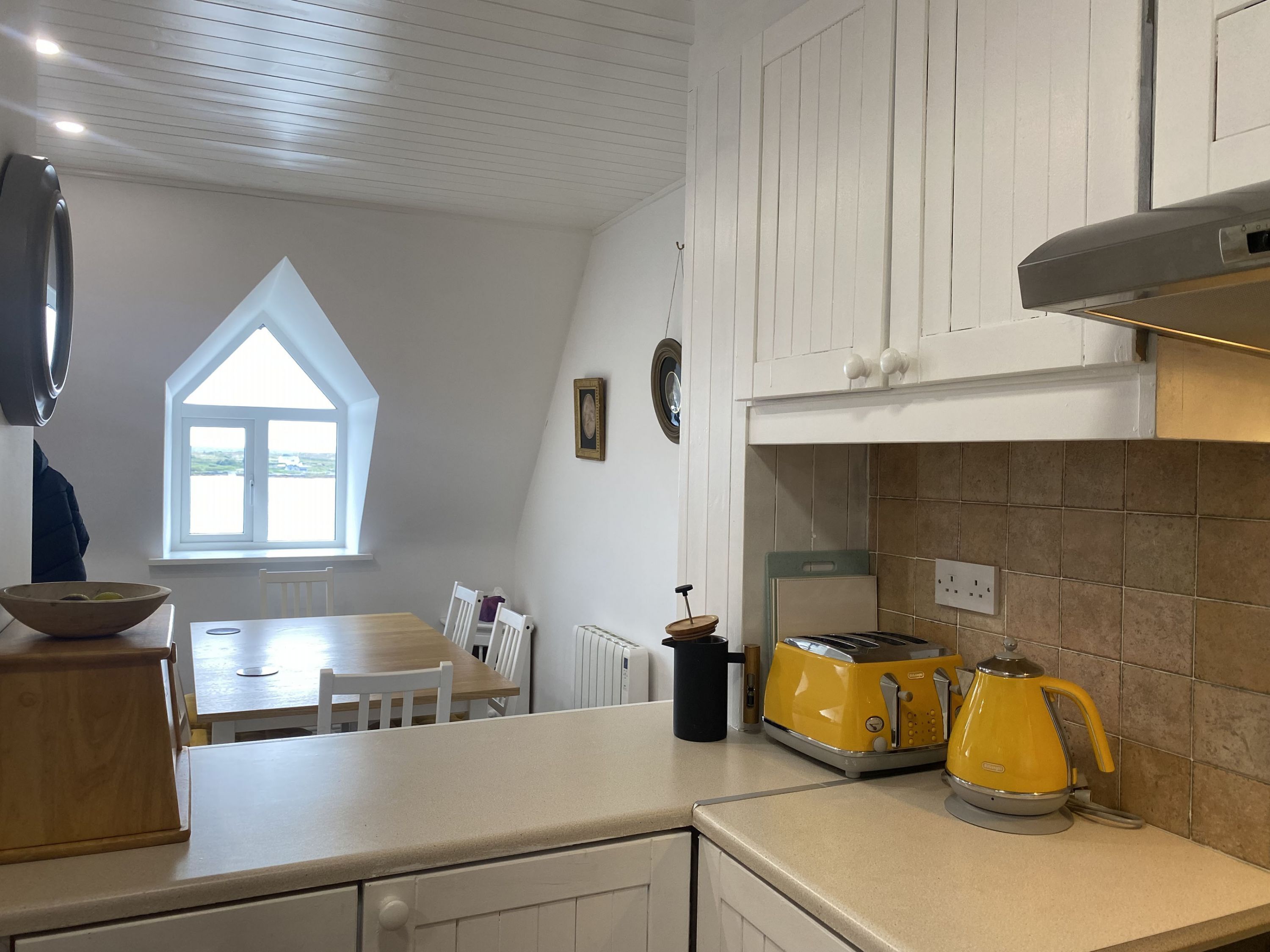 Eine Küche mit weißen Schränken, einem Fenster, einem Esstisch und einem gelben Toaster.