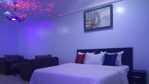 A bedroom with a bed, nightstands, a painting on the wall, and a ceiling light fixture. - Qeesh Quintessential Apartments (Jos)