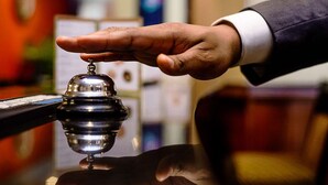 A hand holding a bell, likely in a hotel reception area. - Qeesh Quintessential Apartments (Jos)