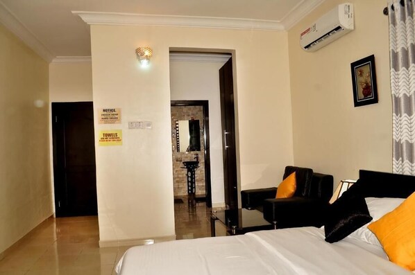 A hotel room with a bed, a black sofa, a small table, and a bathroom visible through an open door.